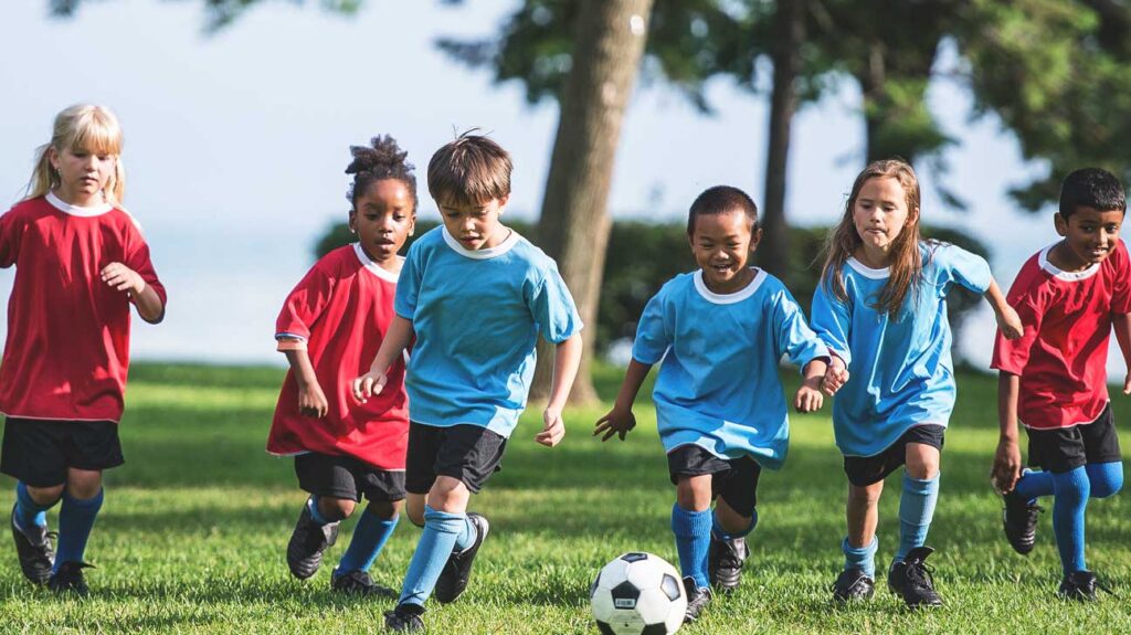 Children playing soccer outside in blue and red jerseys on a sunny day