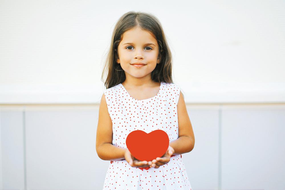 Girl in a white dress holding a red heart indoors