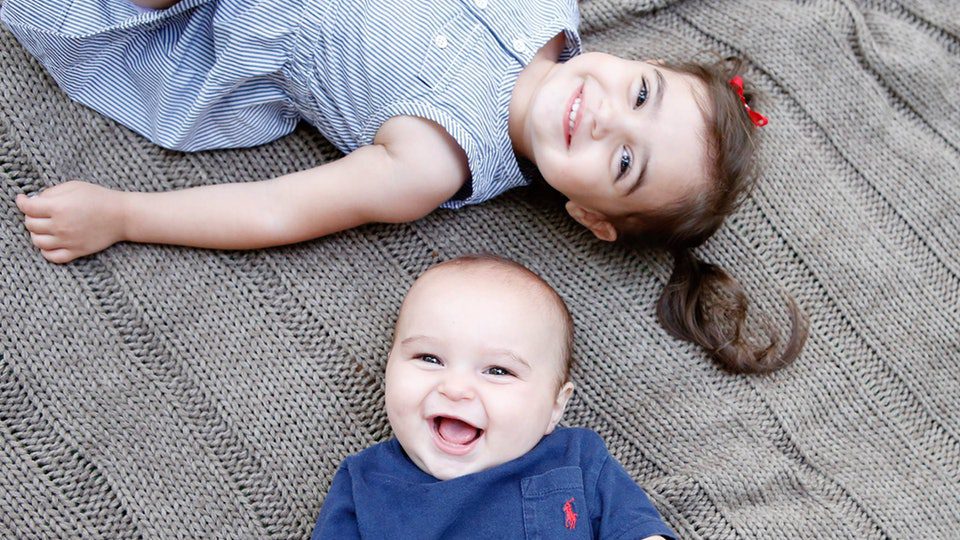 Smiling siblings lying on a knitted blanket in casual outfits