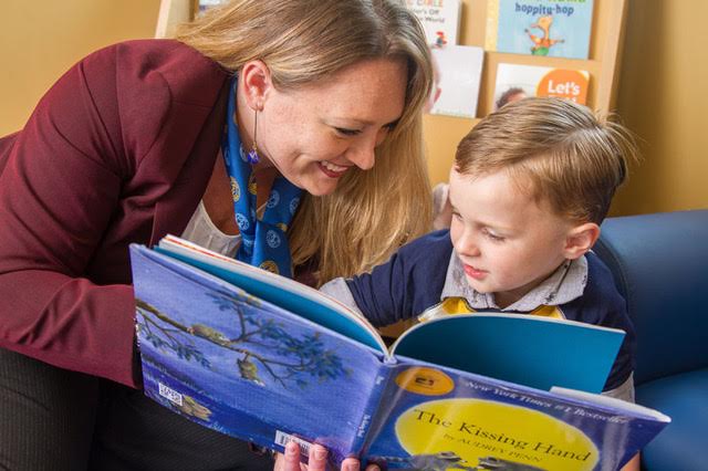 Adult and child reading a book together in a cozy room with bookshelves