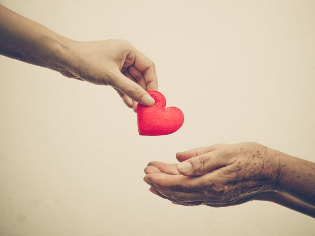 Hand giving a red heart to another in a gesture of kindness and care