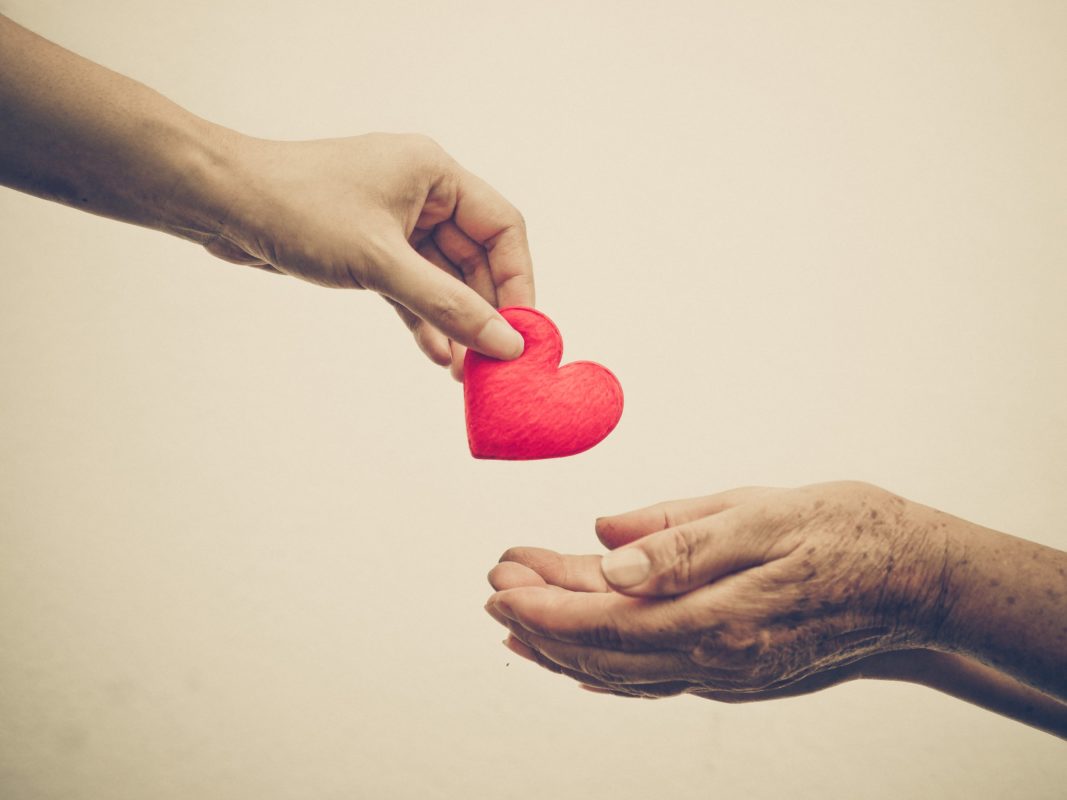 Hand giving a red heart to another in a gesture of kindness and care