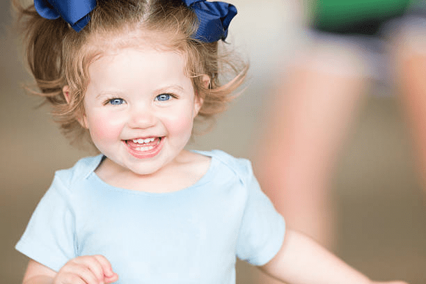 Smiling toddler with blue bows in hair wearing a light blue shirt