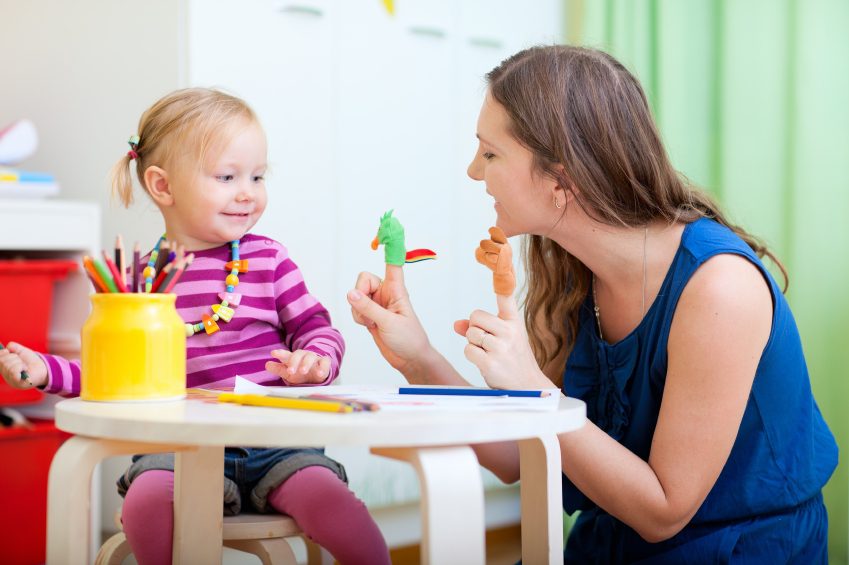 Child and teacher playing with finger puppets at a table