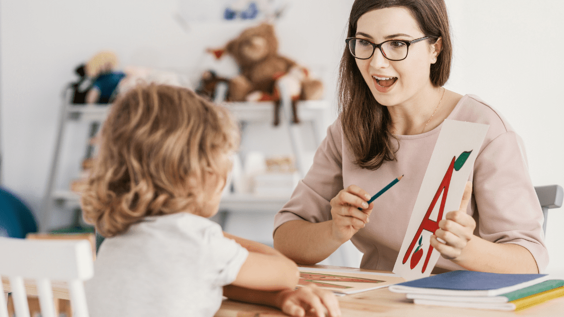 Teacher showing alphabet card to child in classroom setting