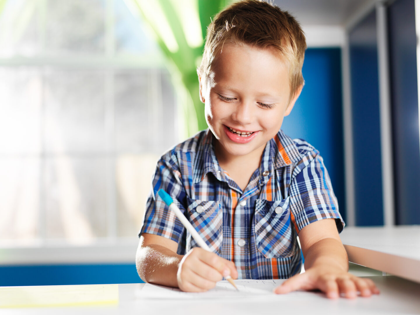 Young boy smiling while writing in a bright classroom