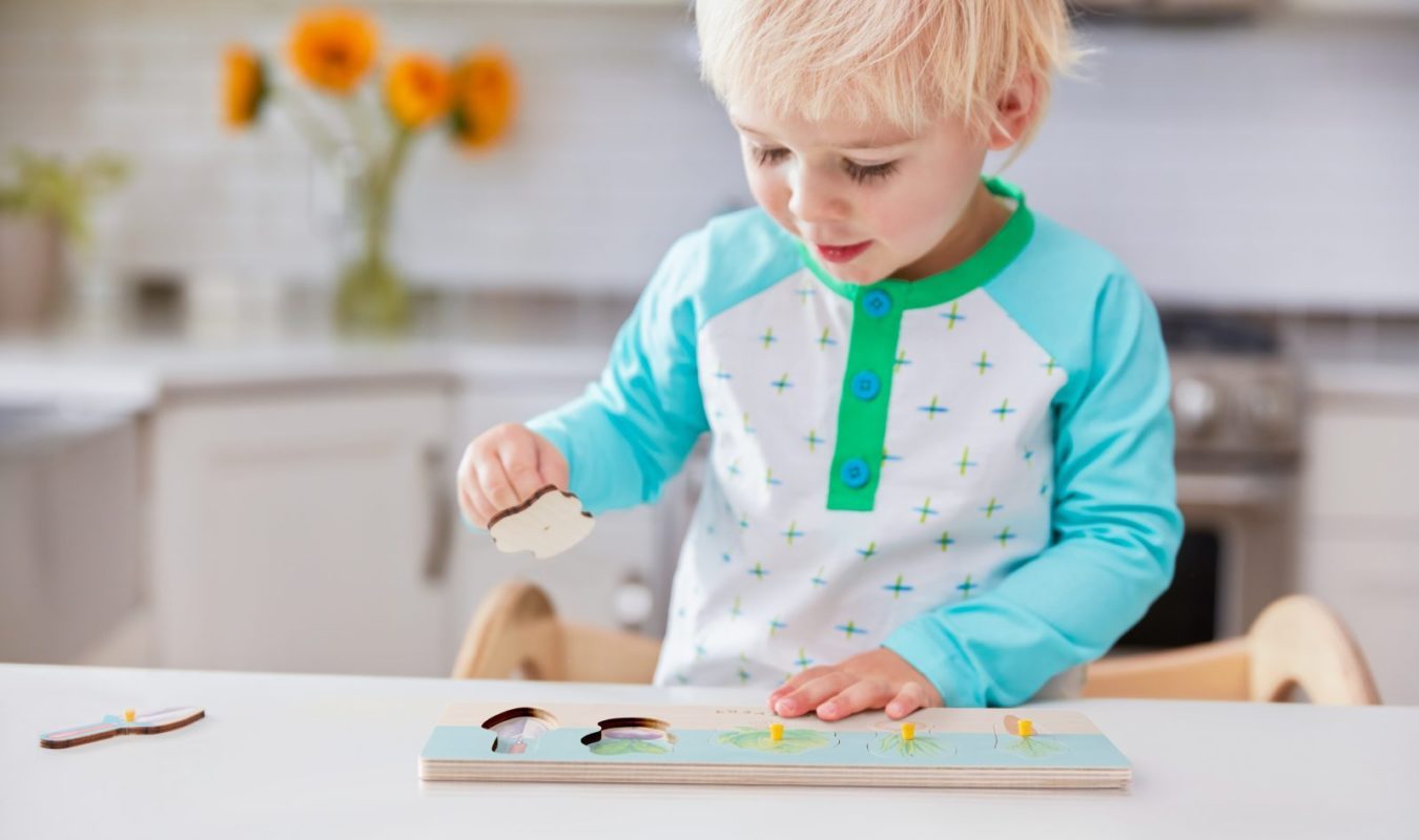 Child playing with a wooden puzzle in a bright kitchen setting