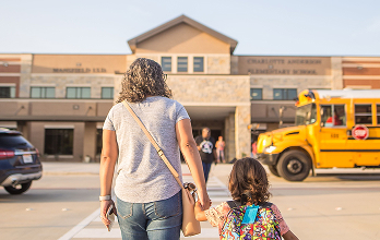 Parent and child walking to school building with school bus nearby