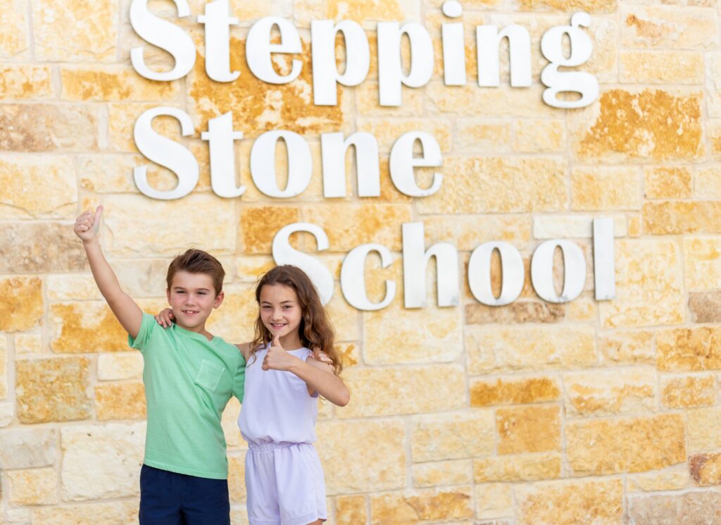 Two happy kids giving thumbs up in front of Stepping Stone School sign