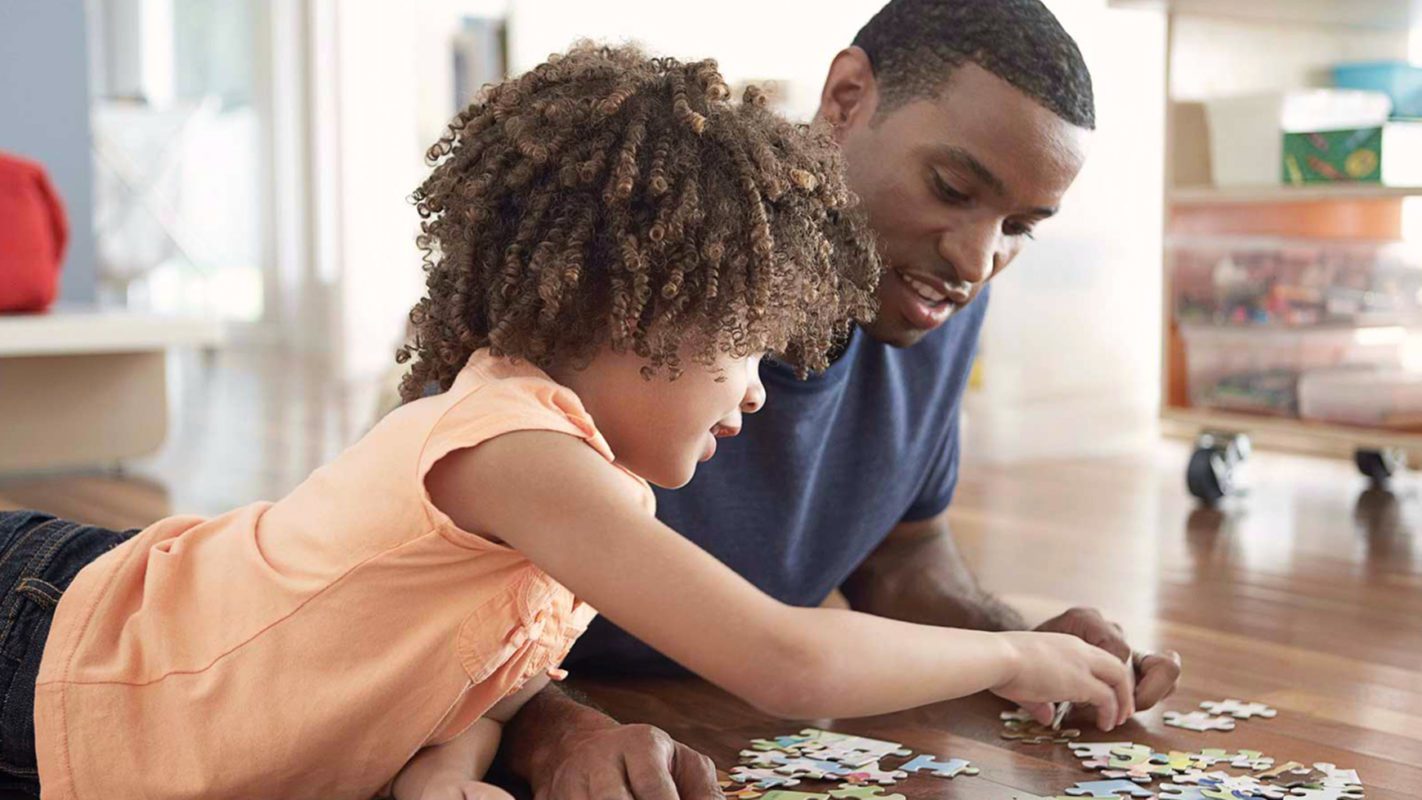 Father and daughter enjoying assembling a jigsaw puzzle together on the floor