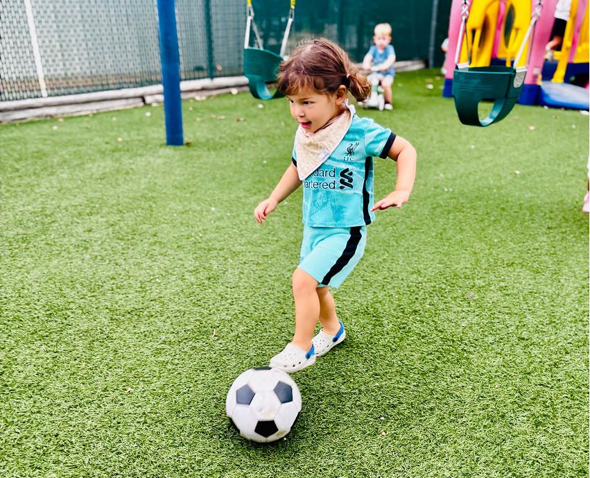 Young child playing soccer on grass playground field in sports jersey.