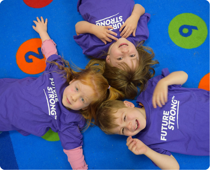 Three children in purple Future Strong shirts lying on a colorful number rug