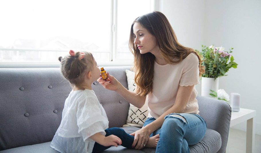 Mother giving daughter essential oil on sofa in bright room