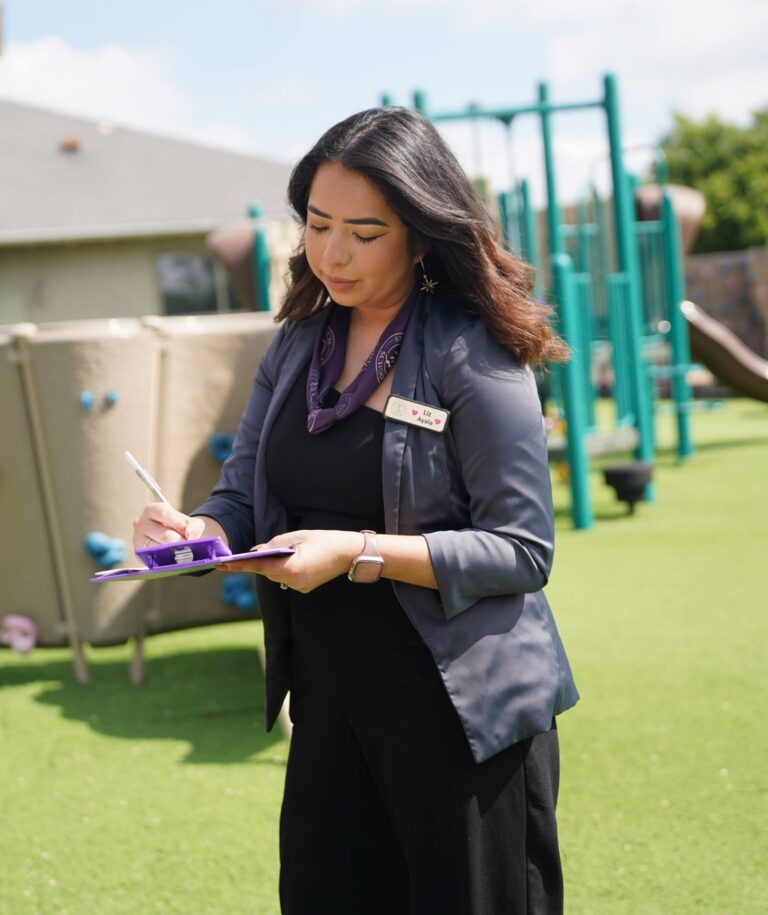 Woman in professional attire taking notes on clipboard at playground
