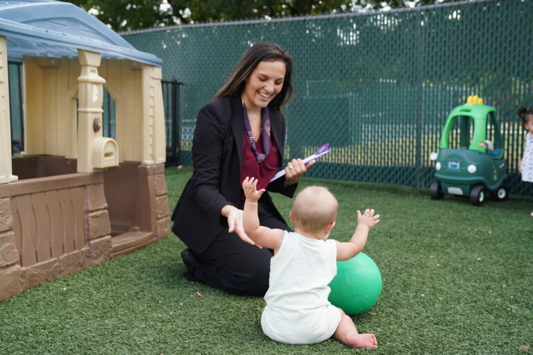 Woman in suit playing with baby holding ball in outdoor playground setting