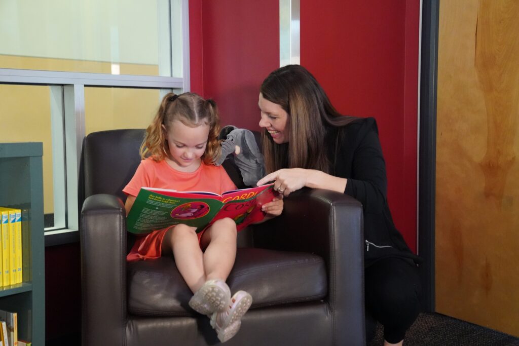 Child and adult reading a book together in a cozy library chair
