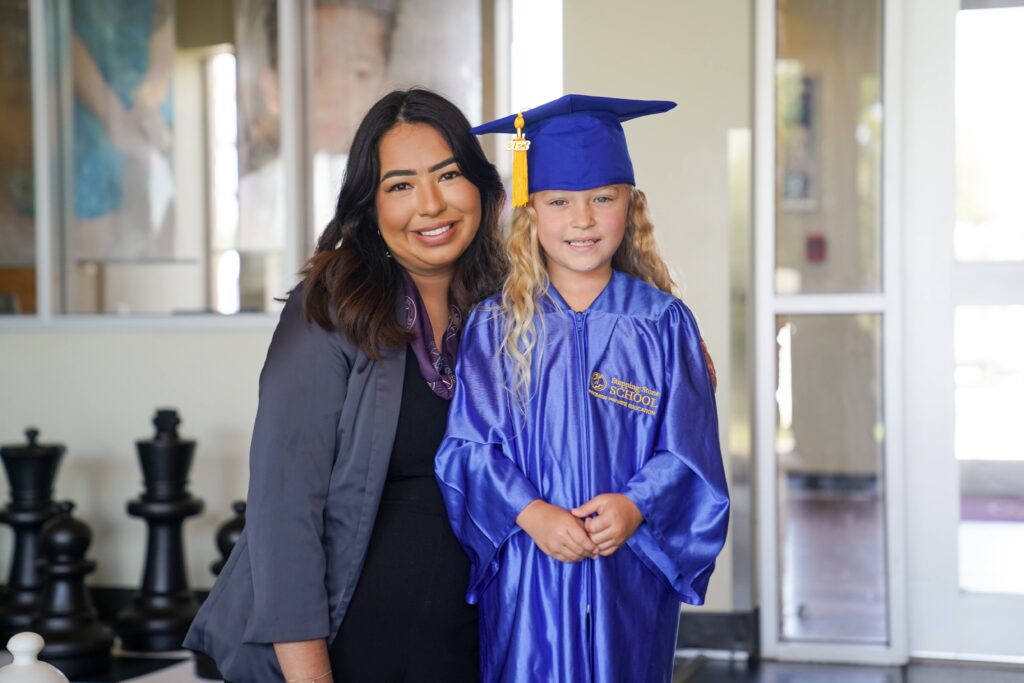 Teacher hugging young graduate in blue cap and gown indoors