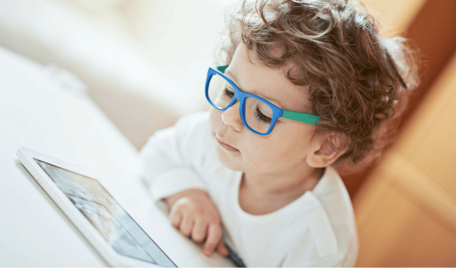 Child with curly hair wearing blue glasses looking at tablet screen