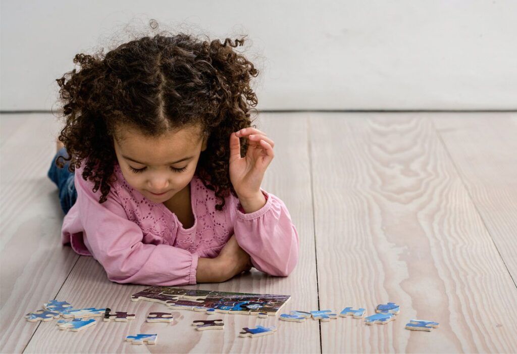 Child in pink shirt solving puzzle on wooden floor