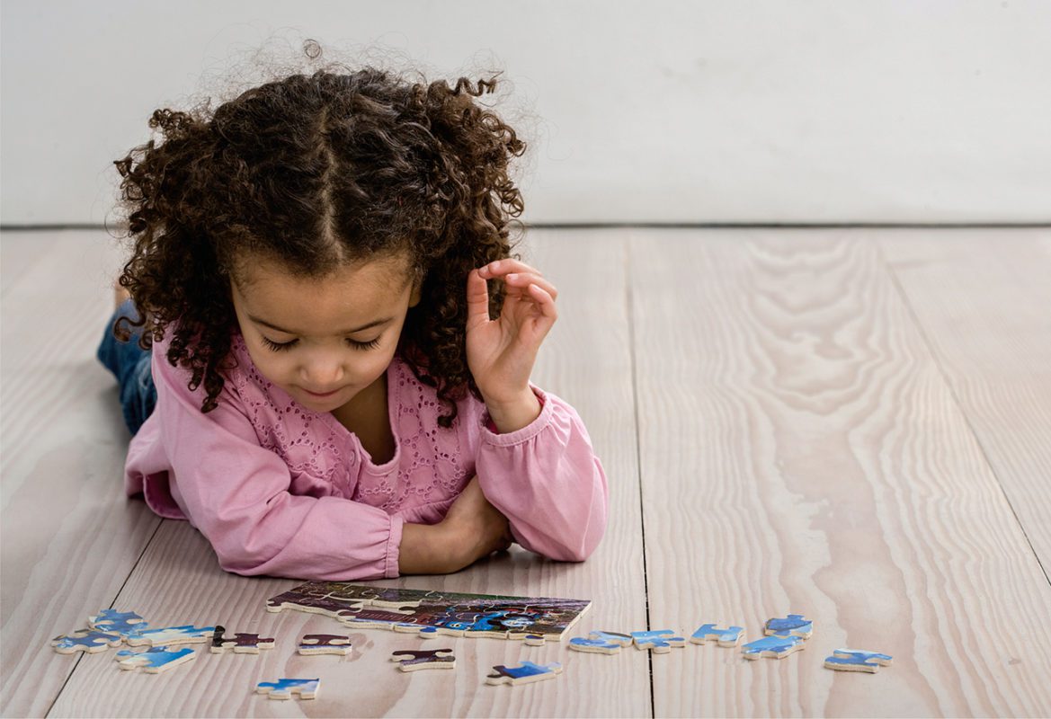 Child in pink shirt solving puzzle on wooden floor