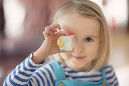 Child holding a colorful geometric paper toy with a playful smile