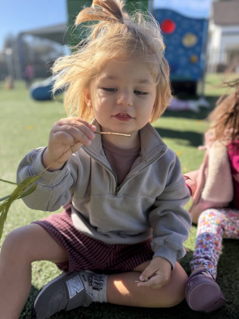 Toddler playing with a twig outdoors on a sunny day