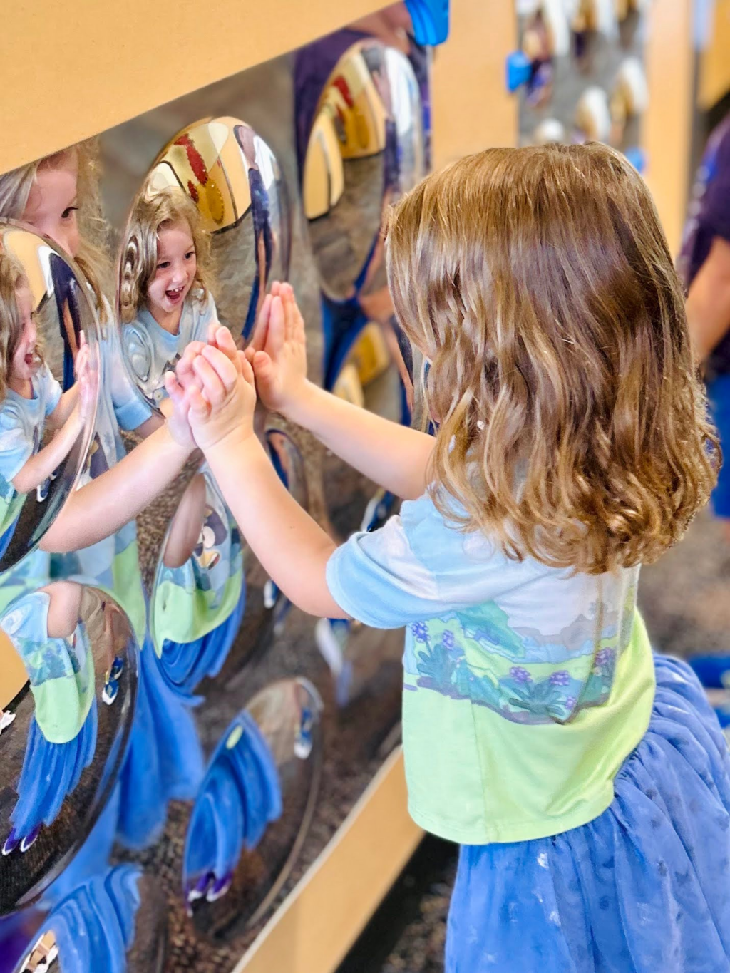 Child playing with a reflective wall at a museum or science center