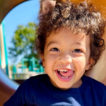 Happy child with curly hair at the playground slide on a sunny day