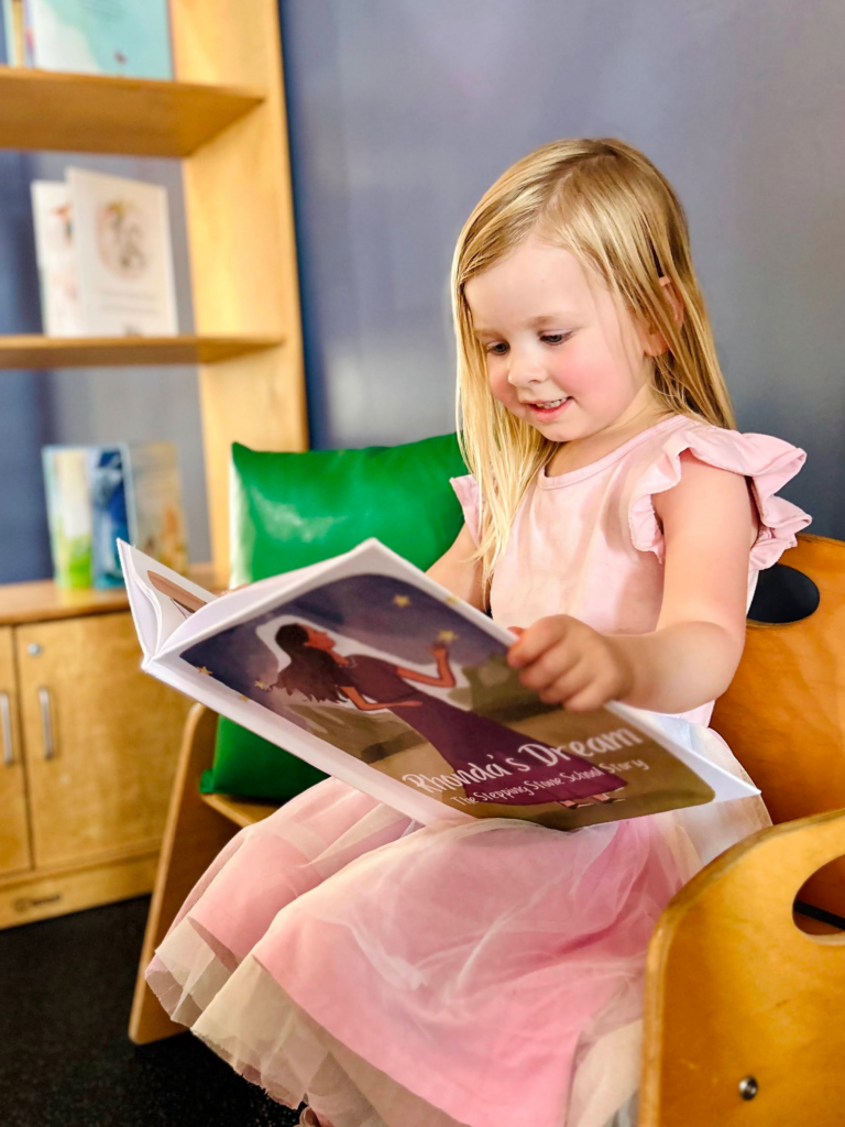 Young girl in pink dress reading a book in a cozy library setting