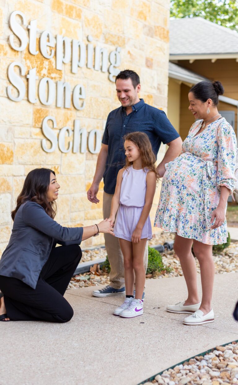 Family visiting Stepping Stone School while a staff member greets a young girl outside the entrance.