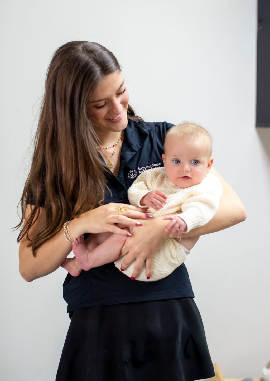 Woman smiling while holding a baby in a cozy sweater indoors