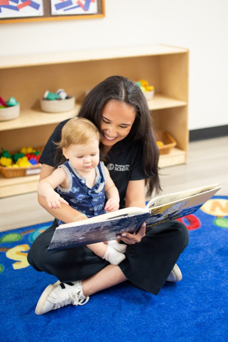 Teacher reading a storybook to a young child in a classroom sitting on a colorful rug