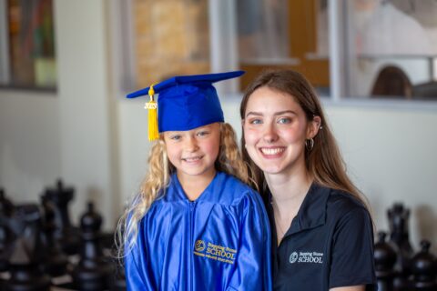 Child in blue graduation gown smiling with a woman in a school setting