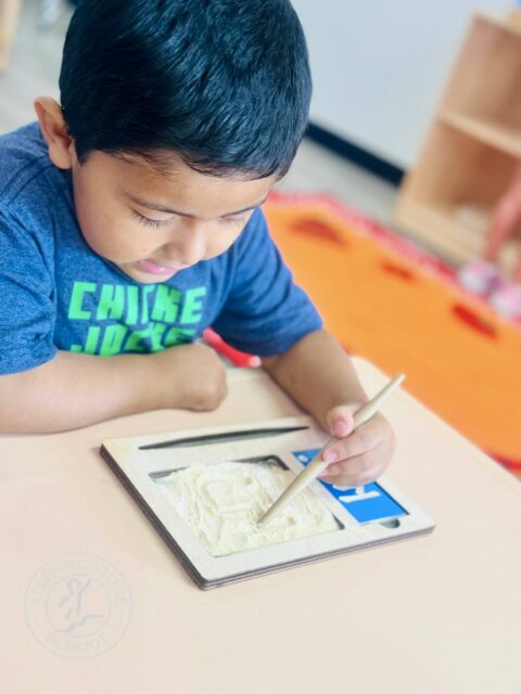 Child practicing writing skills with sand tray at a Montessori school