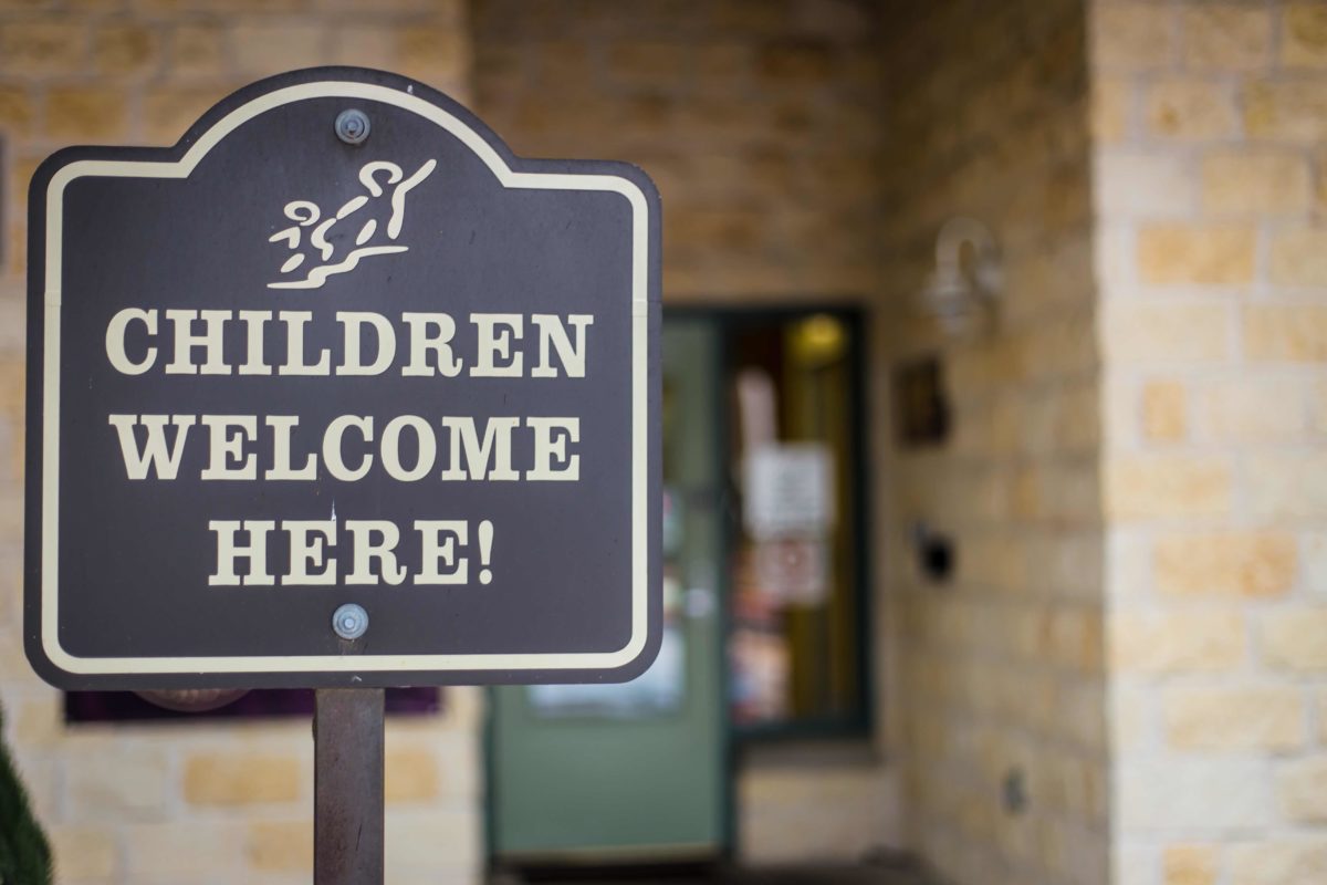Sign reading Children Welcome Here outside a building entrance
