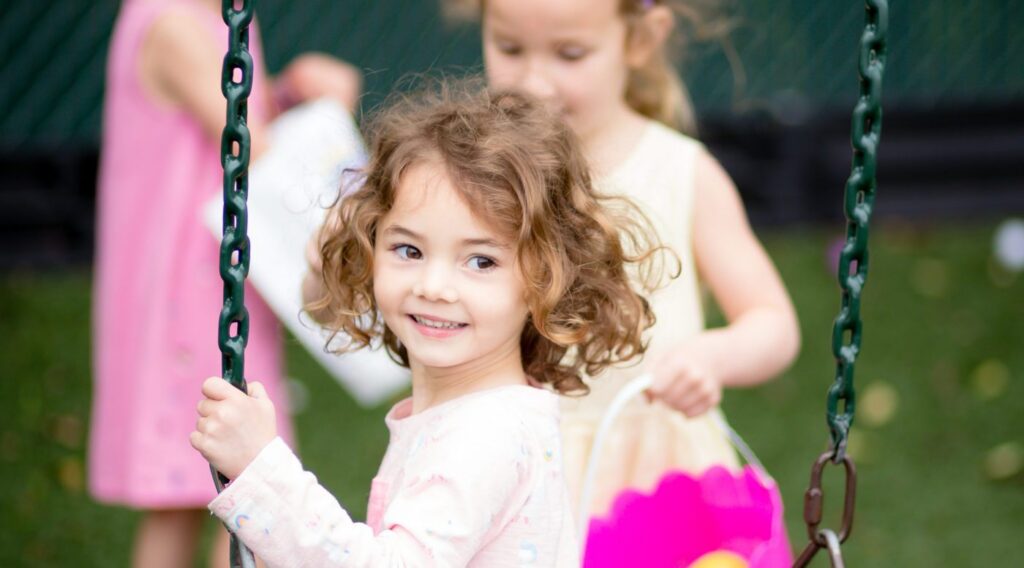 Young girl smiling on swing with friends in playground