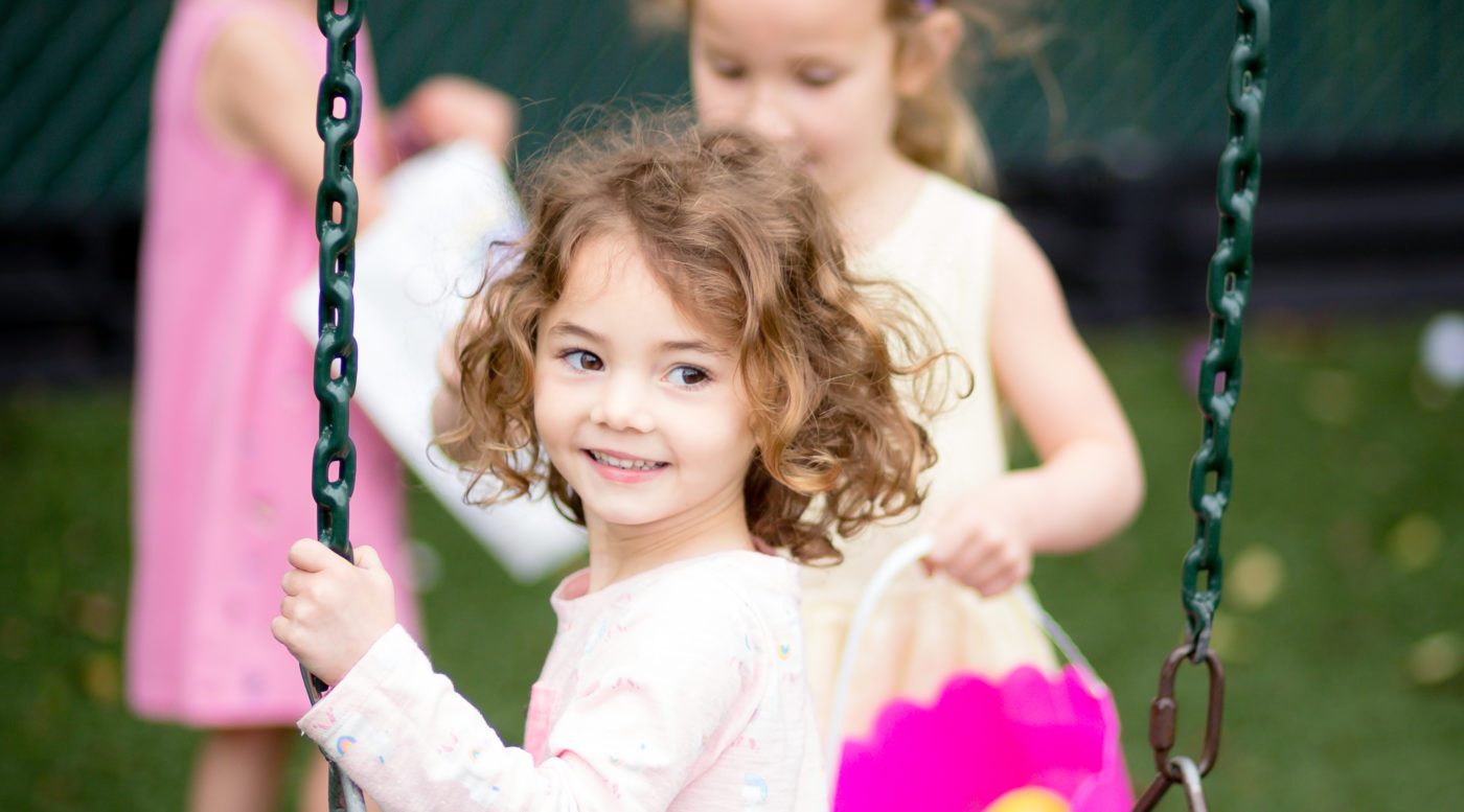 Young girl smiling on swing with friends in playground