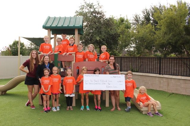 Children and adults in orange shirts posing with a large check on a playground lawn