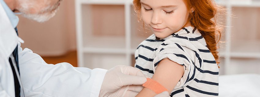 Child receiving a bandage on arm from doctor after vaccination