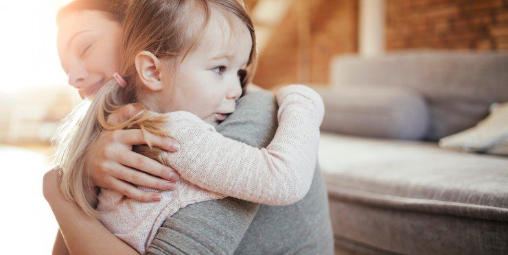 Mother embracing young daughter on a cozy living room couch