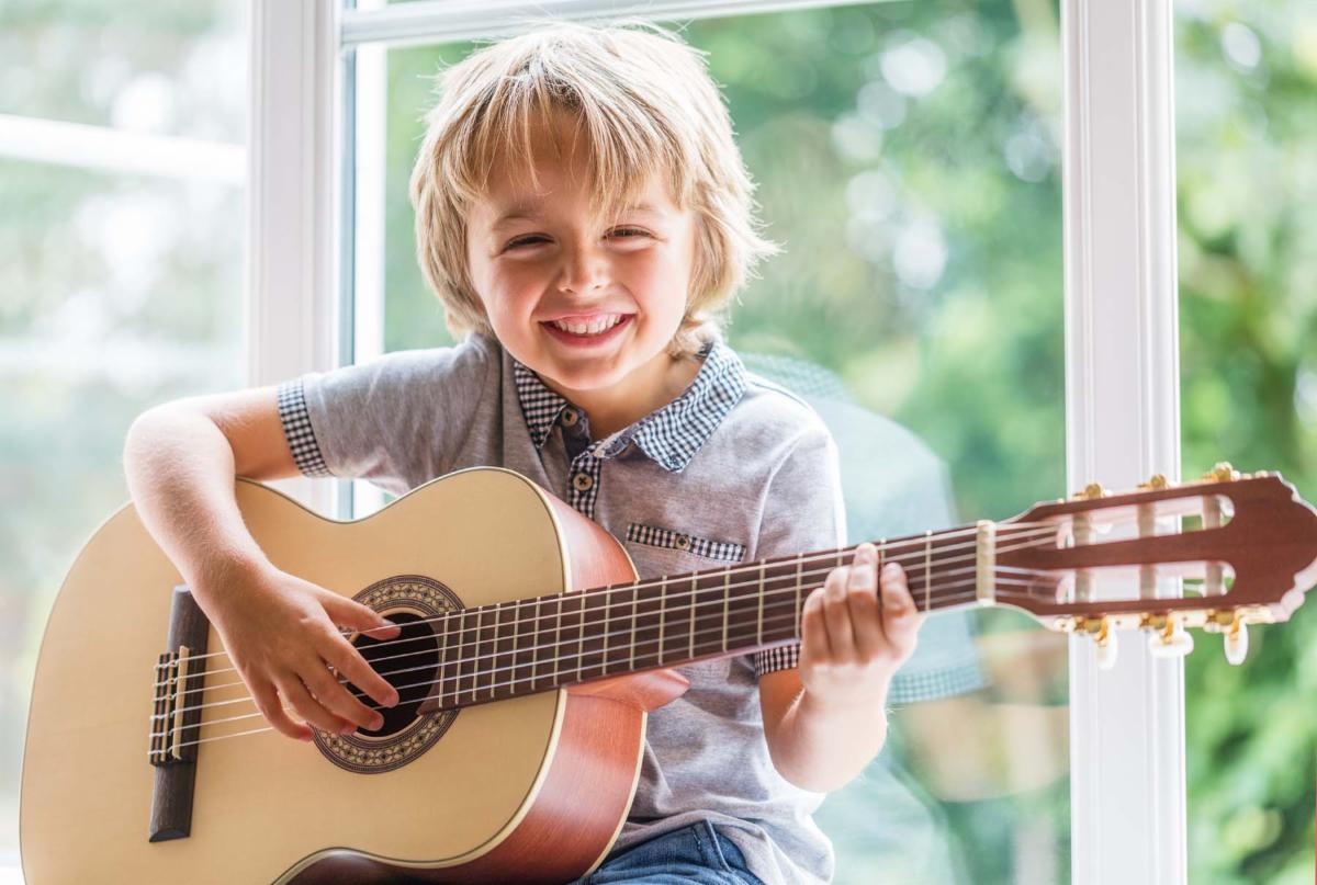 Smiling child playing acoustic guitar by a window