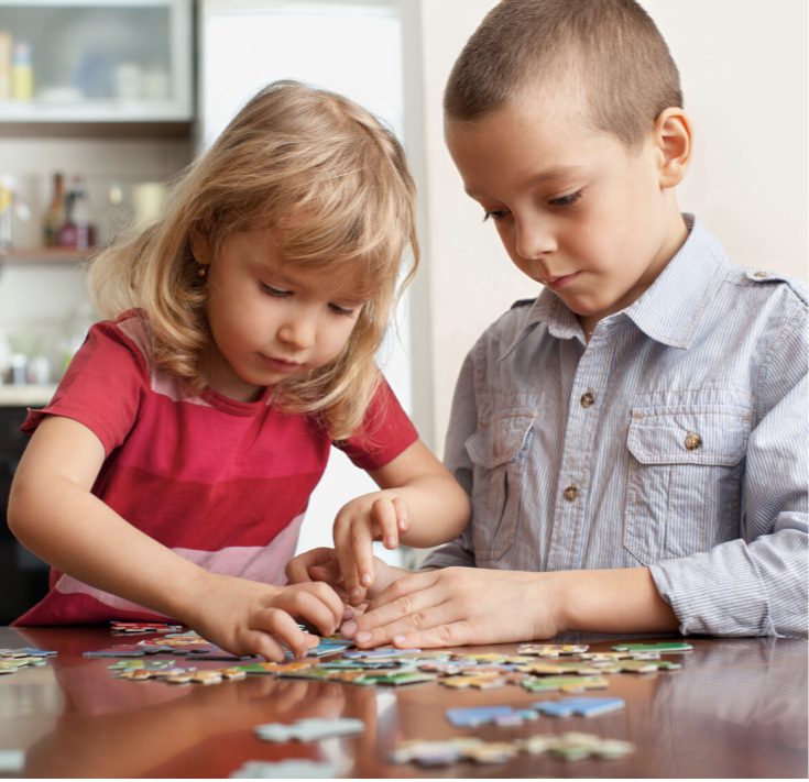 Two children focused on assembling a colorful puzzle together at a wooden table