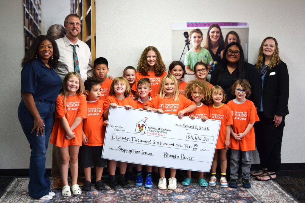 Children in orange shirts holding a large check with adults, Stepping Stone School donation event august 2023.