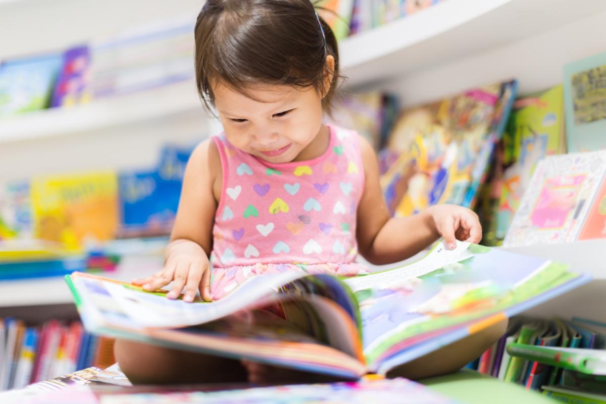 Child joyfully reading a colorful picture book in a library setting