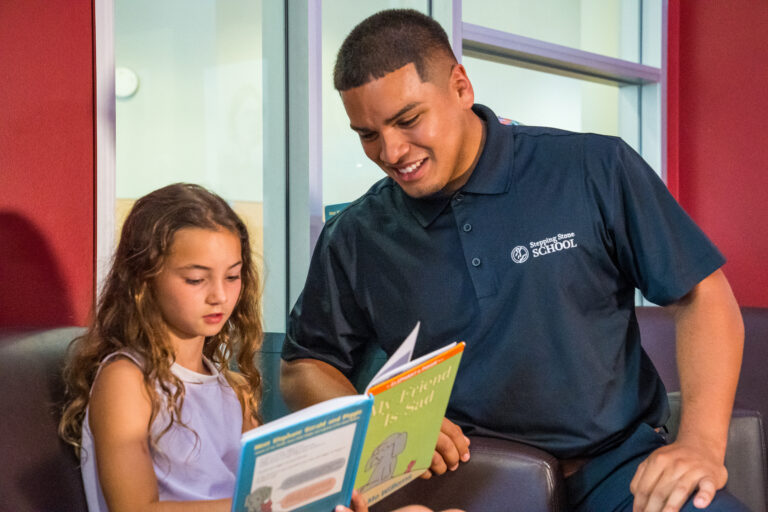 Teacher and young girl reading a book together in a school setting.