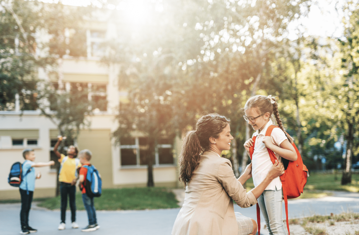 Mother helping daughter with backpack outside school building