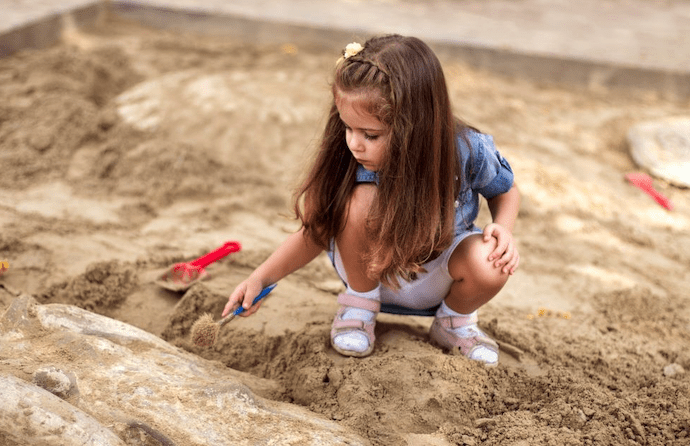 Young girl playing in a sandbox with toy tools during a sunny day outdoors