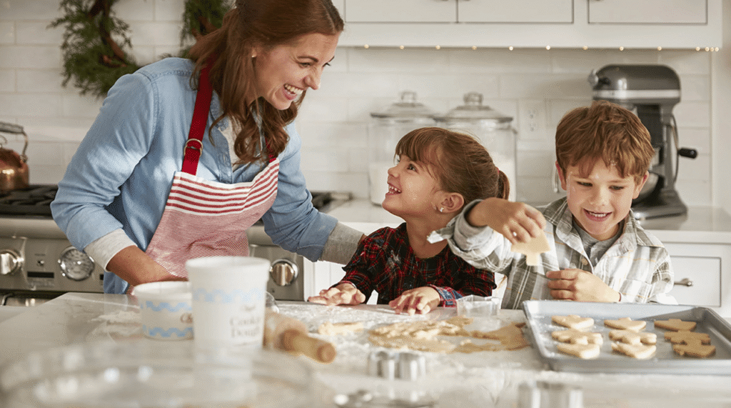 A woman and two children happily baking cookies together in a kitchen