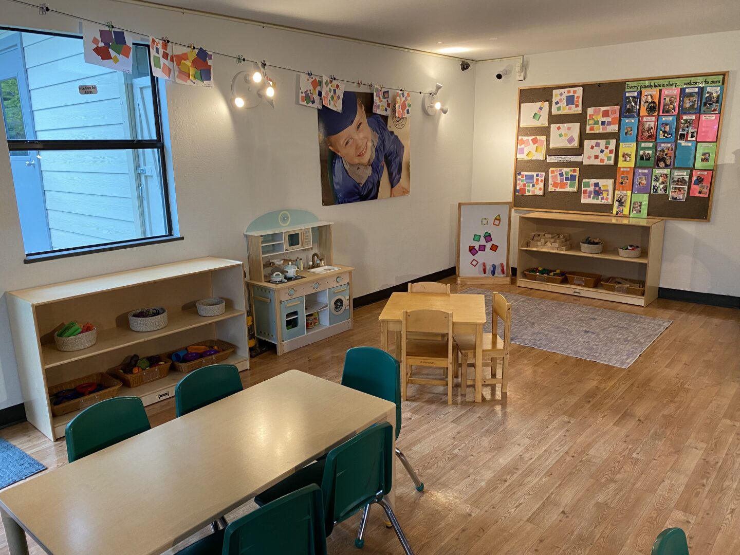 Preschool classroom with tables, chairs, art supplies, and educational displays on walls