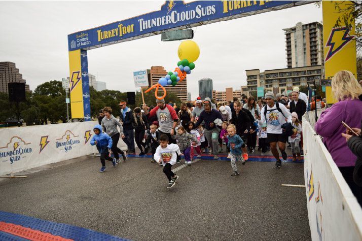 People starting a race at a turkey trot event under an archway with balloons in an urban setting